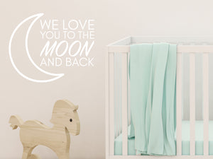 Wall decal for kids in a white color that says ‘We Love You To The Moon And Back’ in a print font  on a kid’s room wall. 