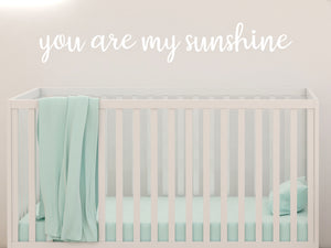 Wall decal for kids in a white color that says ‘You Are My Sunshine’ in a cursive font on a kid’s room wall. 