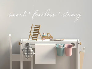 Wall decal for kids in a white color that says ‘Smart Fearless Strong’ in a cursive font on a kid’s room wall. 