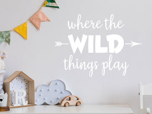 Wall decal for kids in a white color that says ‘Where The Wild Things Play’ with an arrow design on a kid’s room wall. 