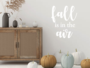 Living room wall decals that say ‘Fall Is In The Air’ in white and a bold font  on a living room wall. 