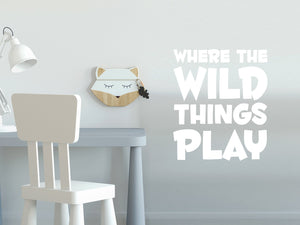 Wall decal for kids in a White color that says ‘Where The Wild Things Play’ in a bold font on a kid’s room wall. 